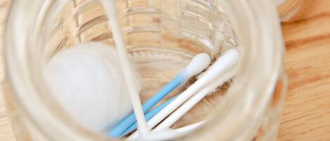 A clear glass jar with cotton swabs and a cotton ball on a wooden surface.