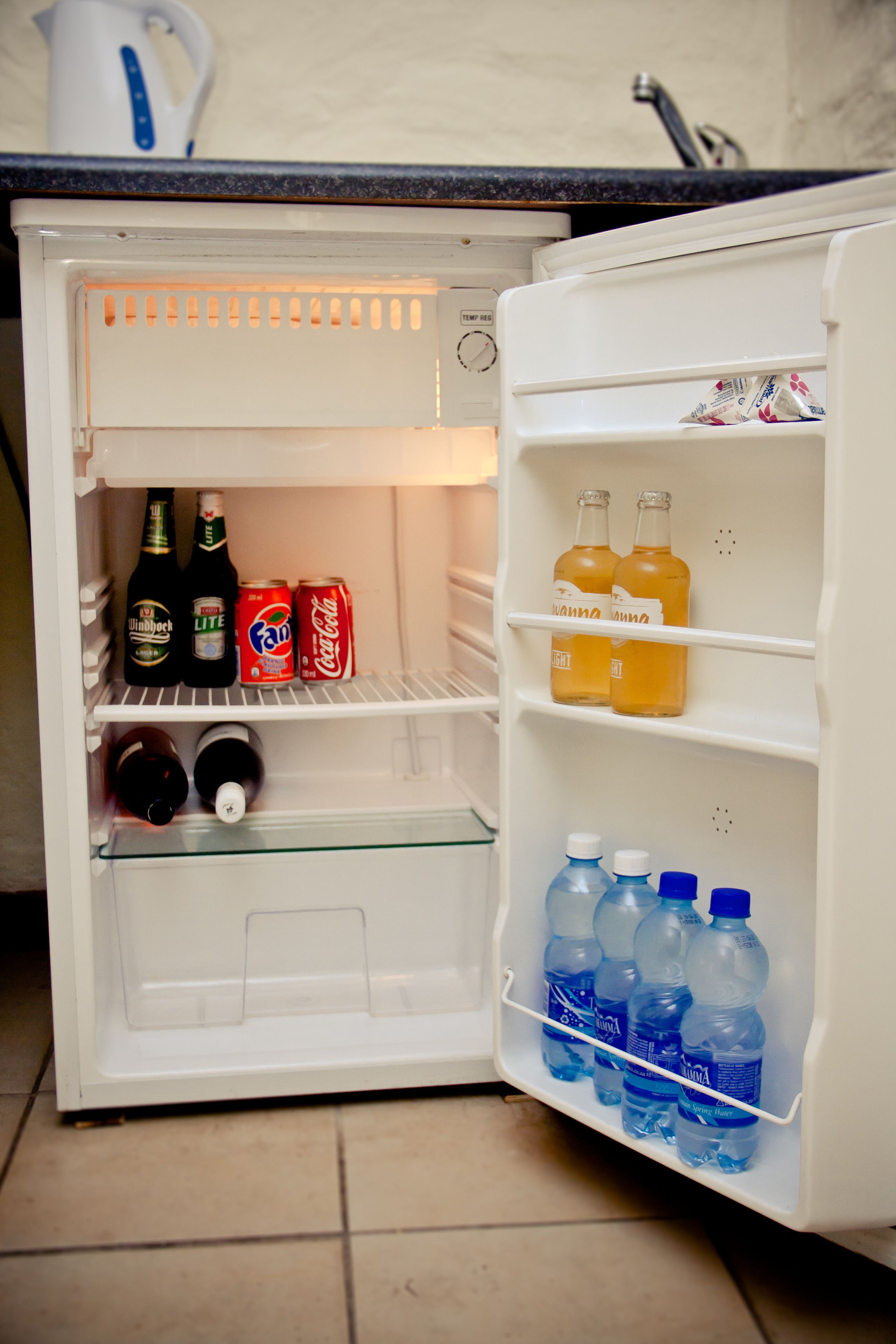 Un réfrigérateur ouvert, dont les étagères contiennent diverses boissons et une bouteille de vin.