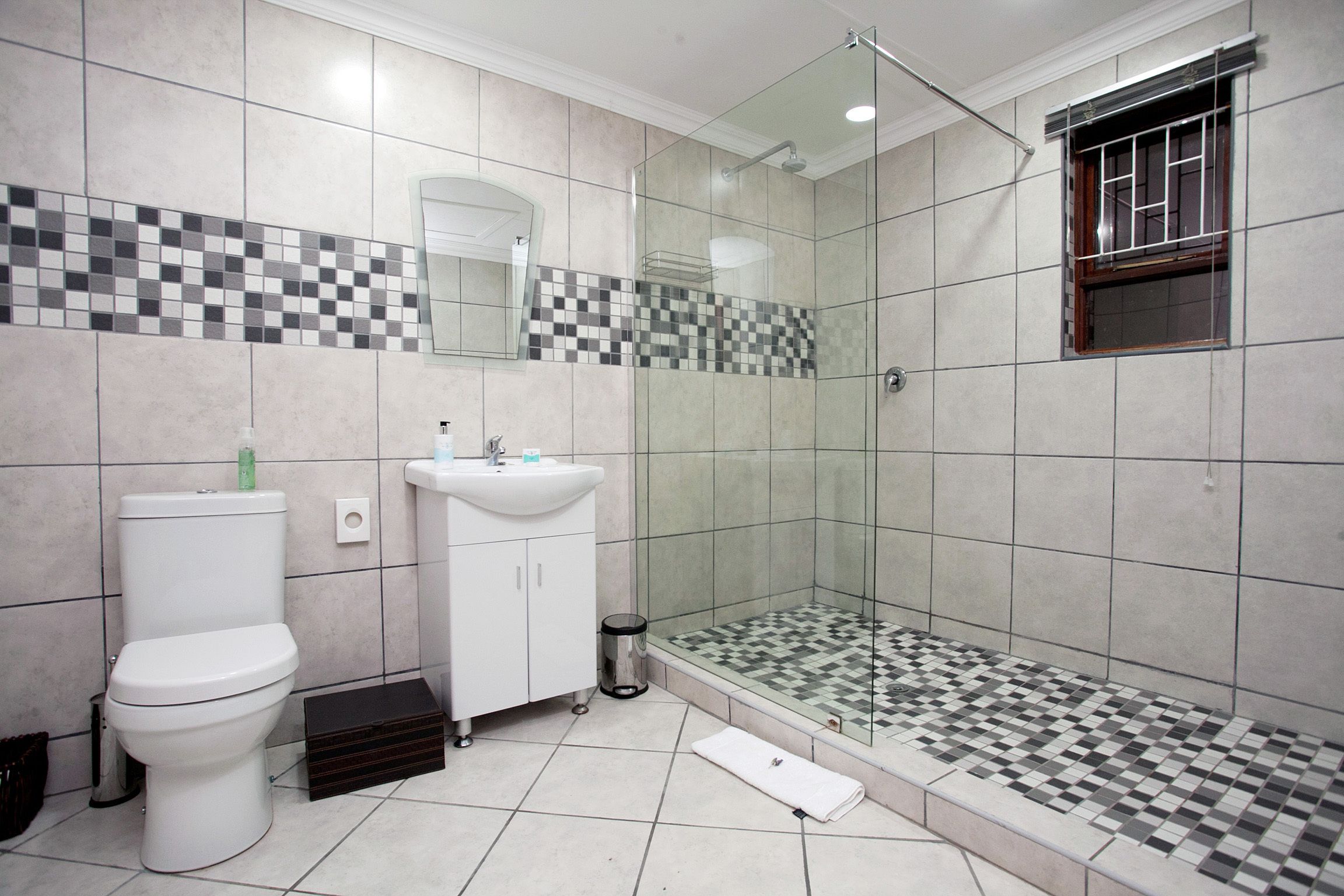 Une salle de bain comprenant des toilettes, un lavabo et une douche séparée par une paroi en verre.