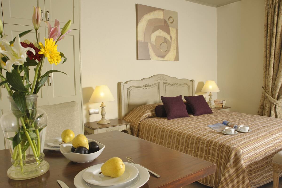 A hotel room with a bed, bedside tables, a dining table with plates and a vase of flowers.