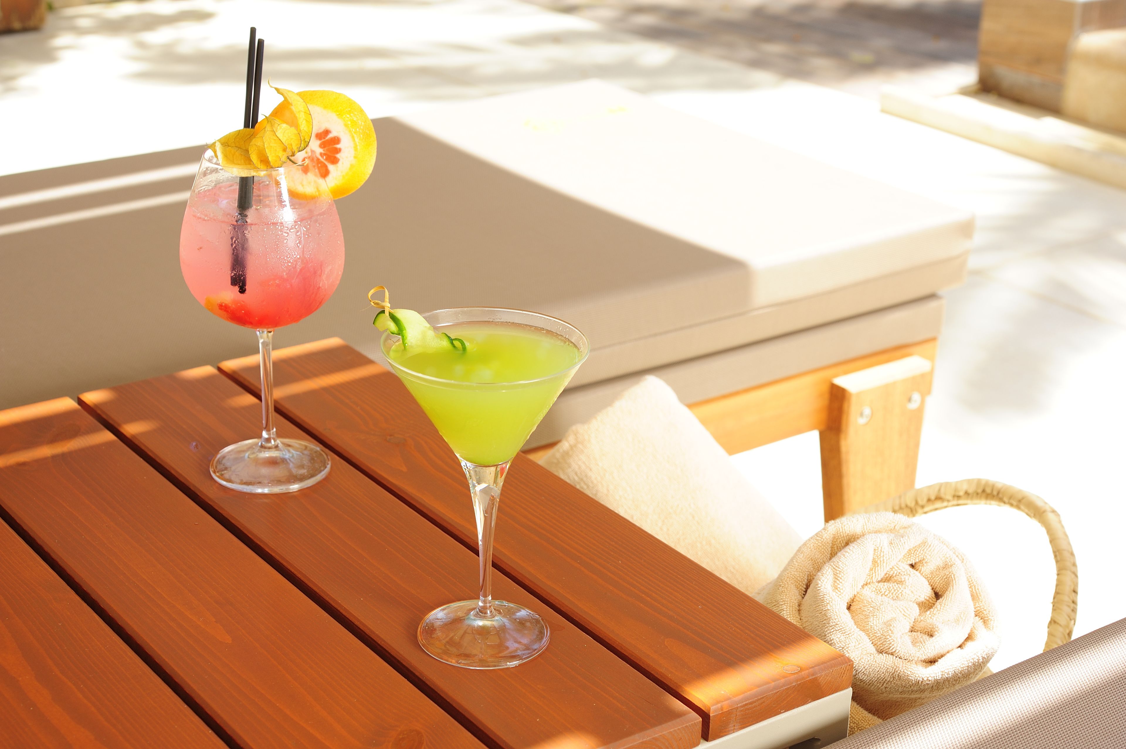 Zwei Cocktails auf einem Holztisch, im Hintergrund ein Korbwannen und ein Kissen.