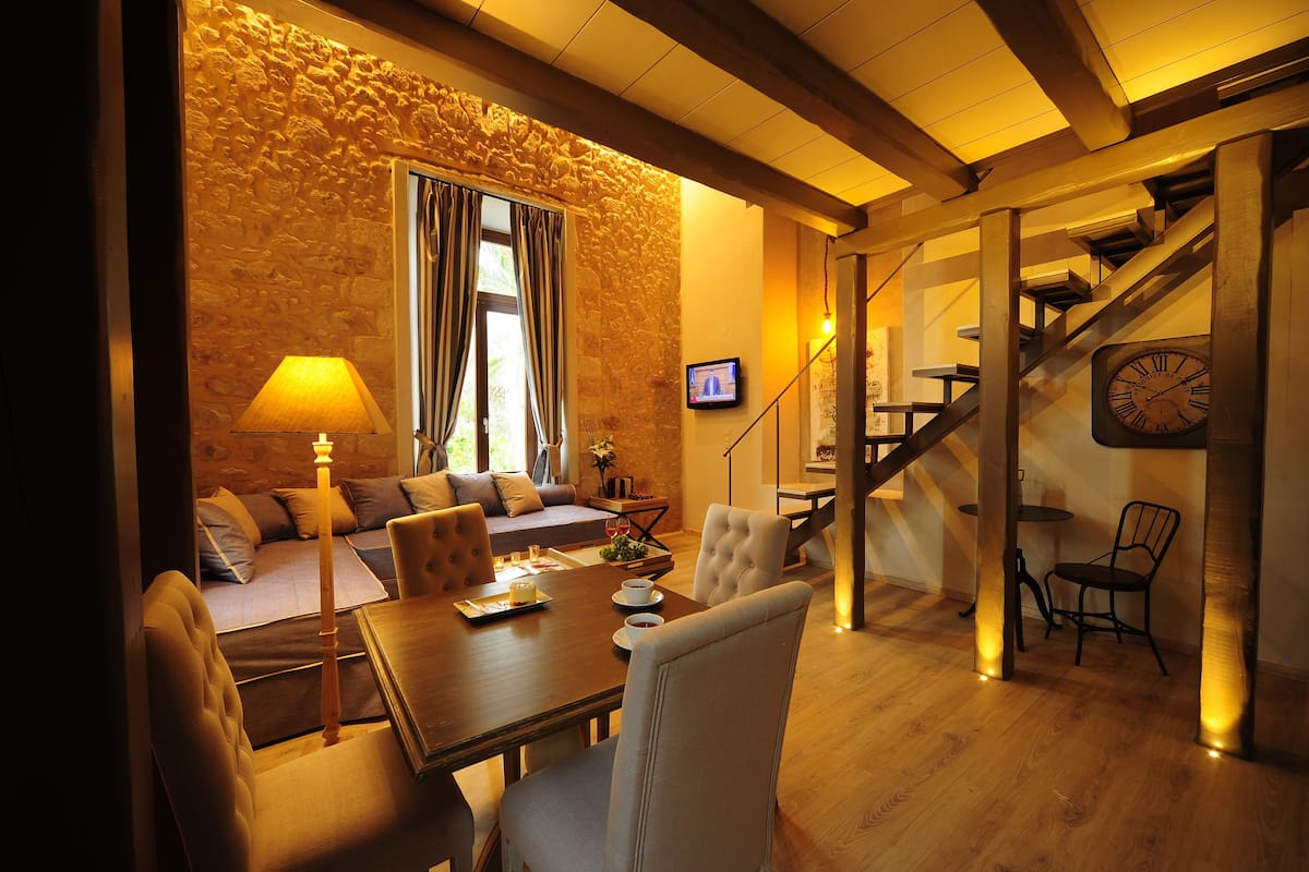 A cozy living area with a stone wall, a sofa, a dining table, and a staircase.
