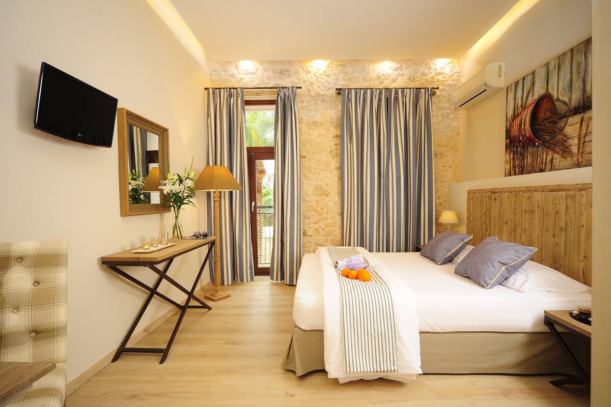 A bedroom with a bed, a TV, a desk, and a window with curtains.