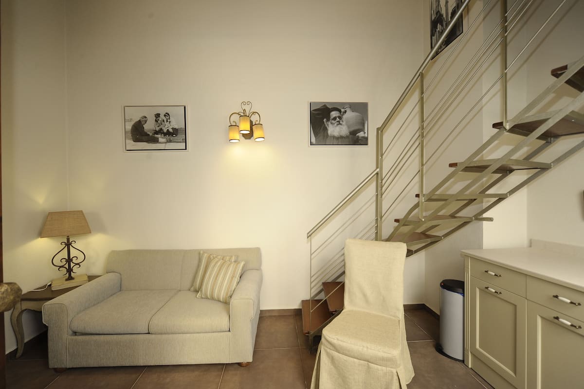 A living room with a sofa, a chair, a lamp, a staircase, and two framed pictures on the wall.