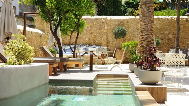 Un área de piscina con sillones de descanso, una mesa y una pequeña fuente de agua.