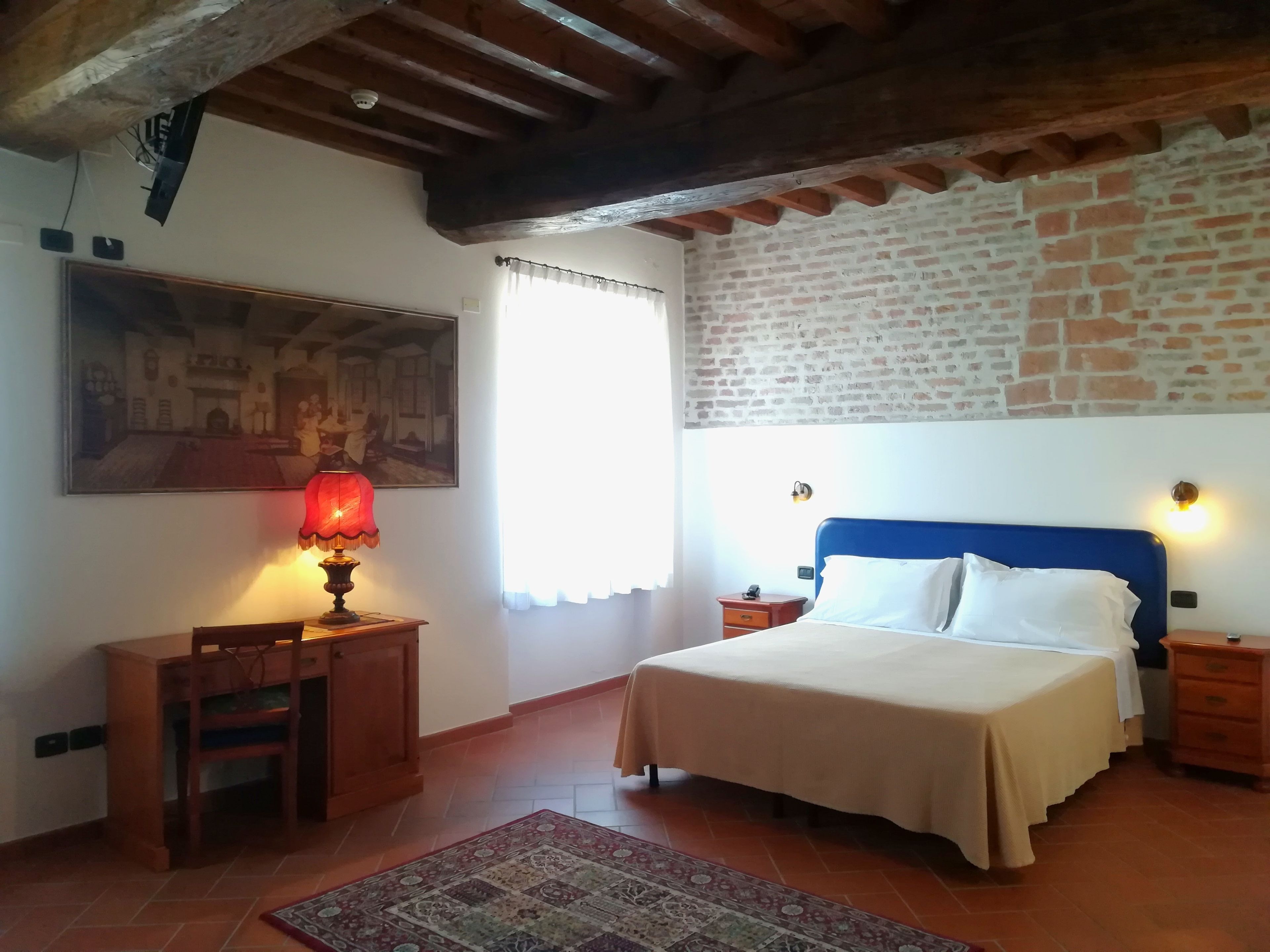 A bedroom with a bed, a nightstand, a lamp, a chair, a rug, and a painting on the wall.