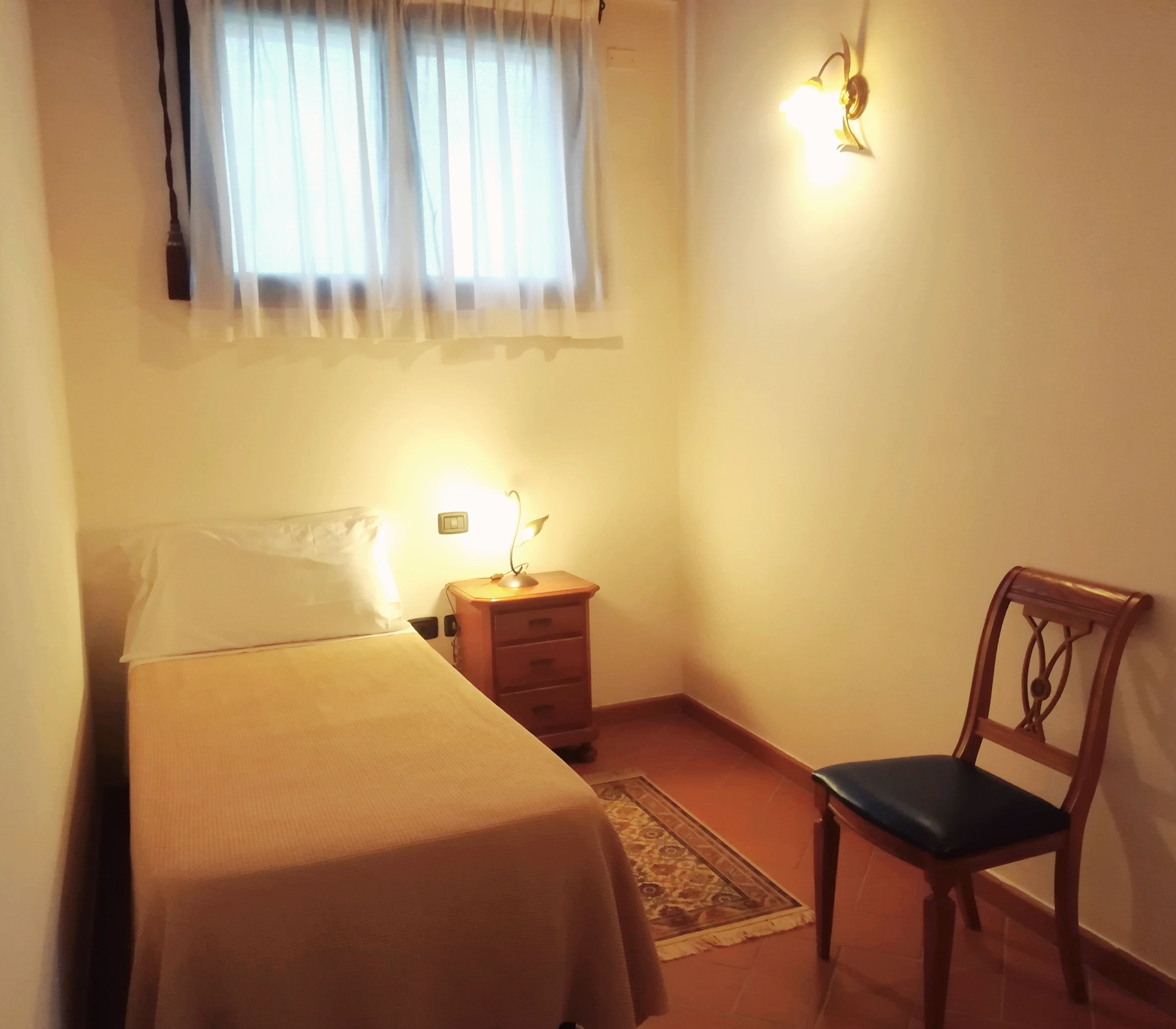 Ein kleiner, gemütlicher Raum mit einem Bett, einem Nachttisch, einem Sessel und einer Wandleuchte.