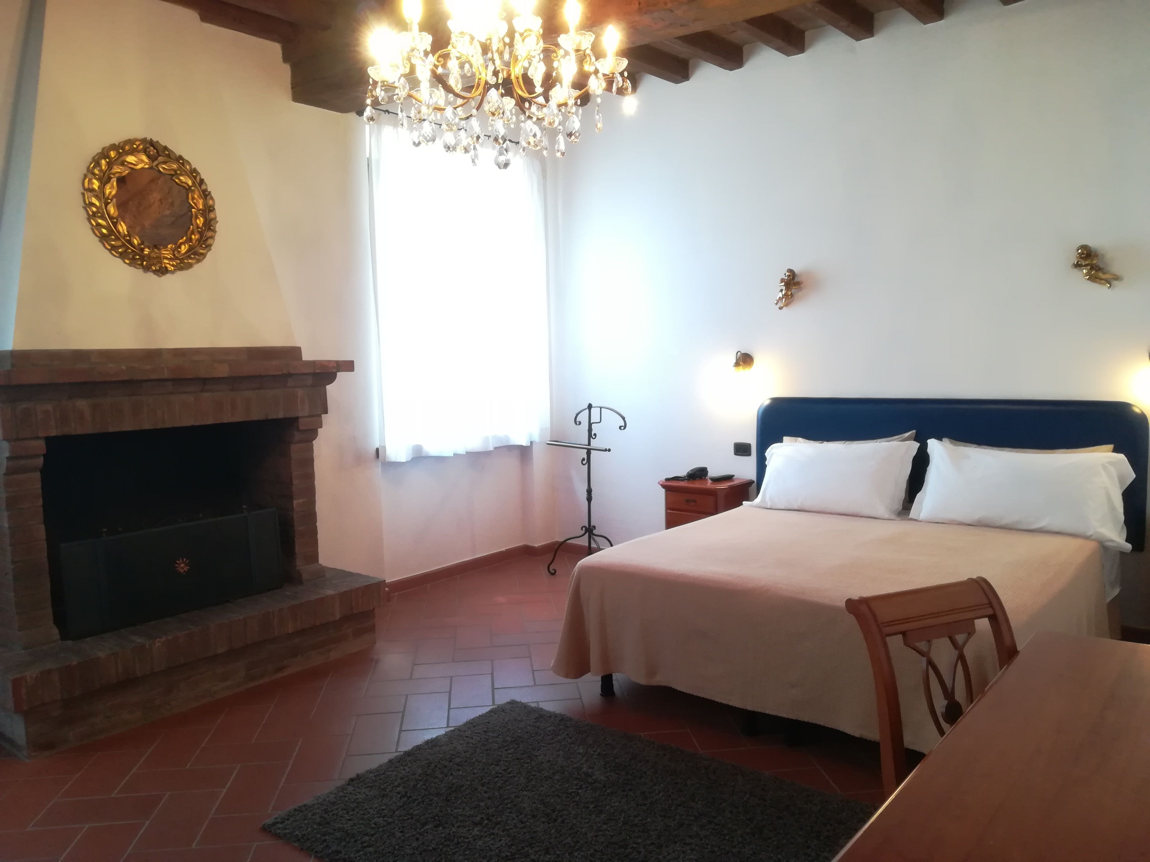 A bedroom with a fireplace, a bed with white bedding, a wooden table, and a chandelier.