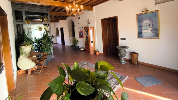 Un pasillo amplio con vigas de madera, un candelabro, plantas en macetas y un cuadro en la pared.