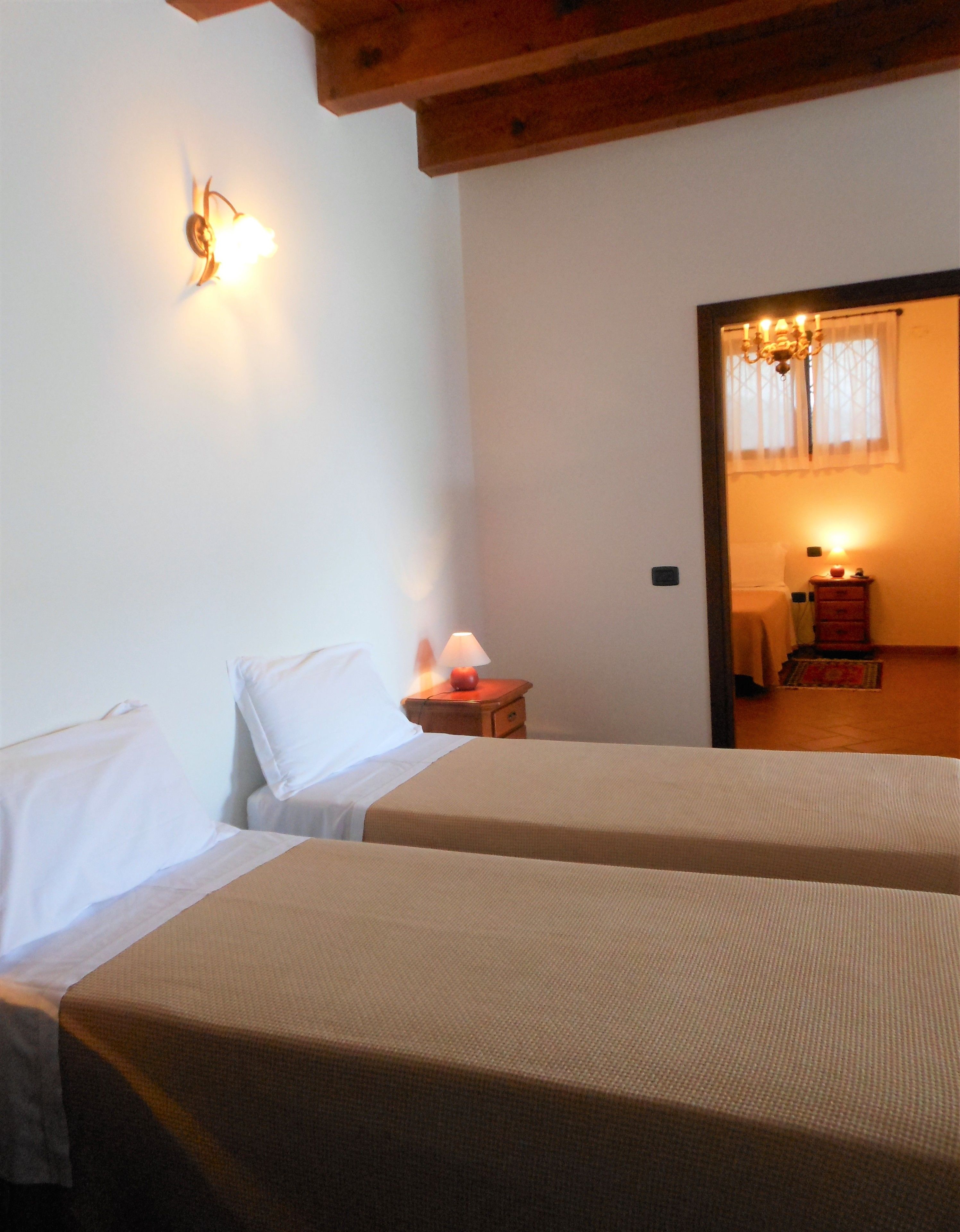A hotel room with two beds, a nightstand with a lamp, and a wooden ceiling.