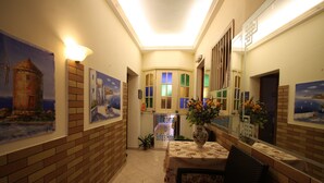 A hallway with brick walls, framed artwork, a reception desk with a vase of flowers, and a sign welcoming guests to Sofia's Hotel. - Sofia Pension (Rhodes)
