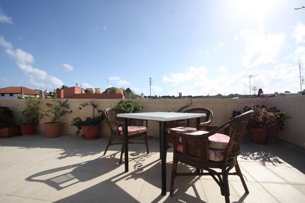A rooftop patio with a table and chairs, surrounded by potted plants.
