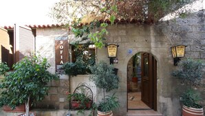 A stone building with a sign for "SOFIA ROOMS LET". There are potted plants and a tiled ground. - Sofia Pension (Rhodes)