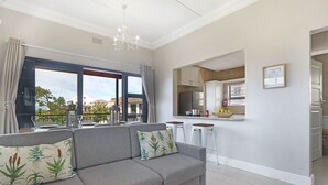 A modern living room with a grey sofa, a chandelier, and a kitchen area with a refrigerator and counter. - Star Holiday Apartments (Cape Town)