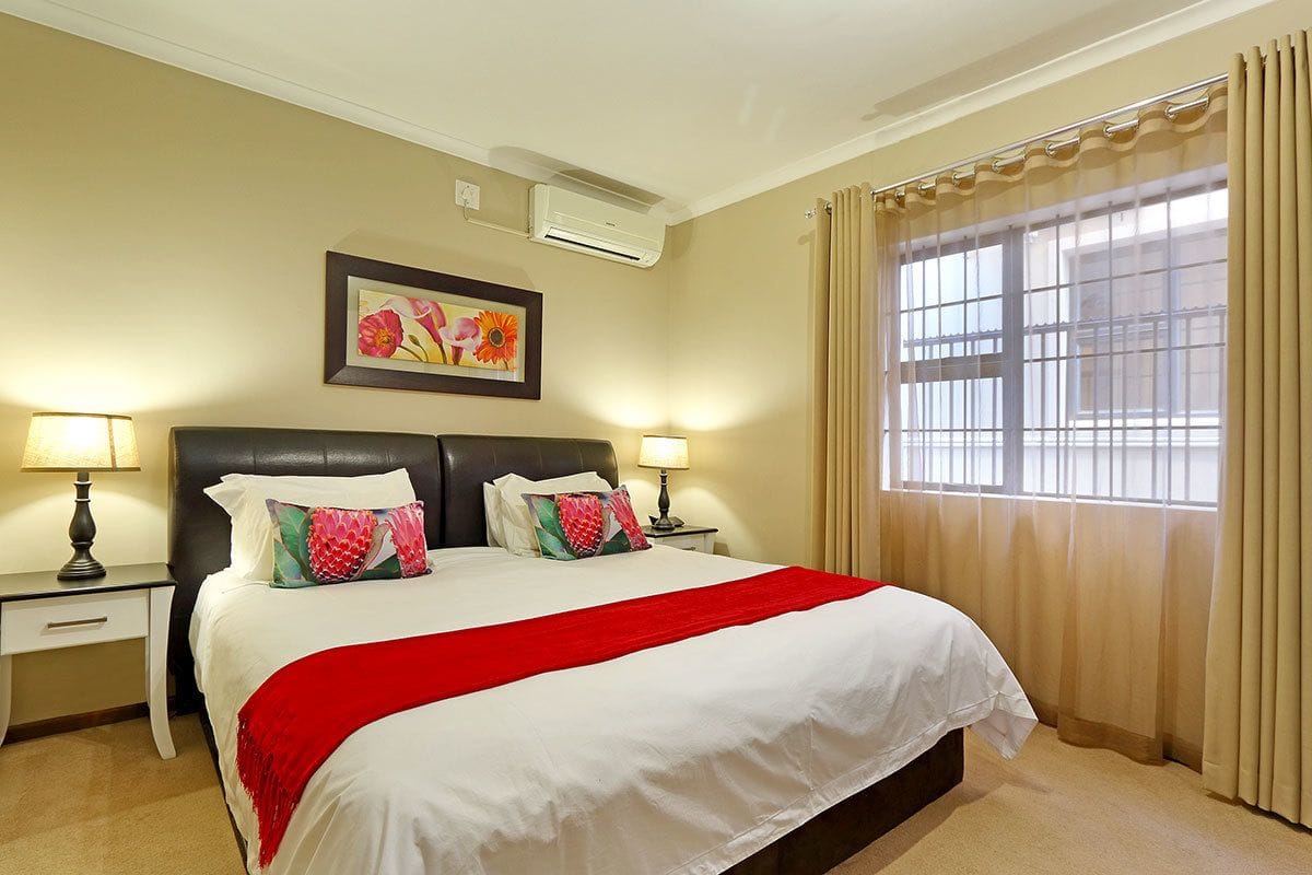 A hotel room with a large bed, two bedside tables with lamps, a window with curtains, and an air conditioning unit on the wall.