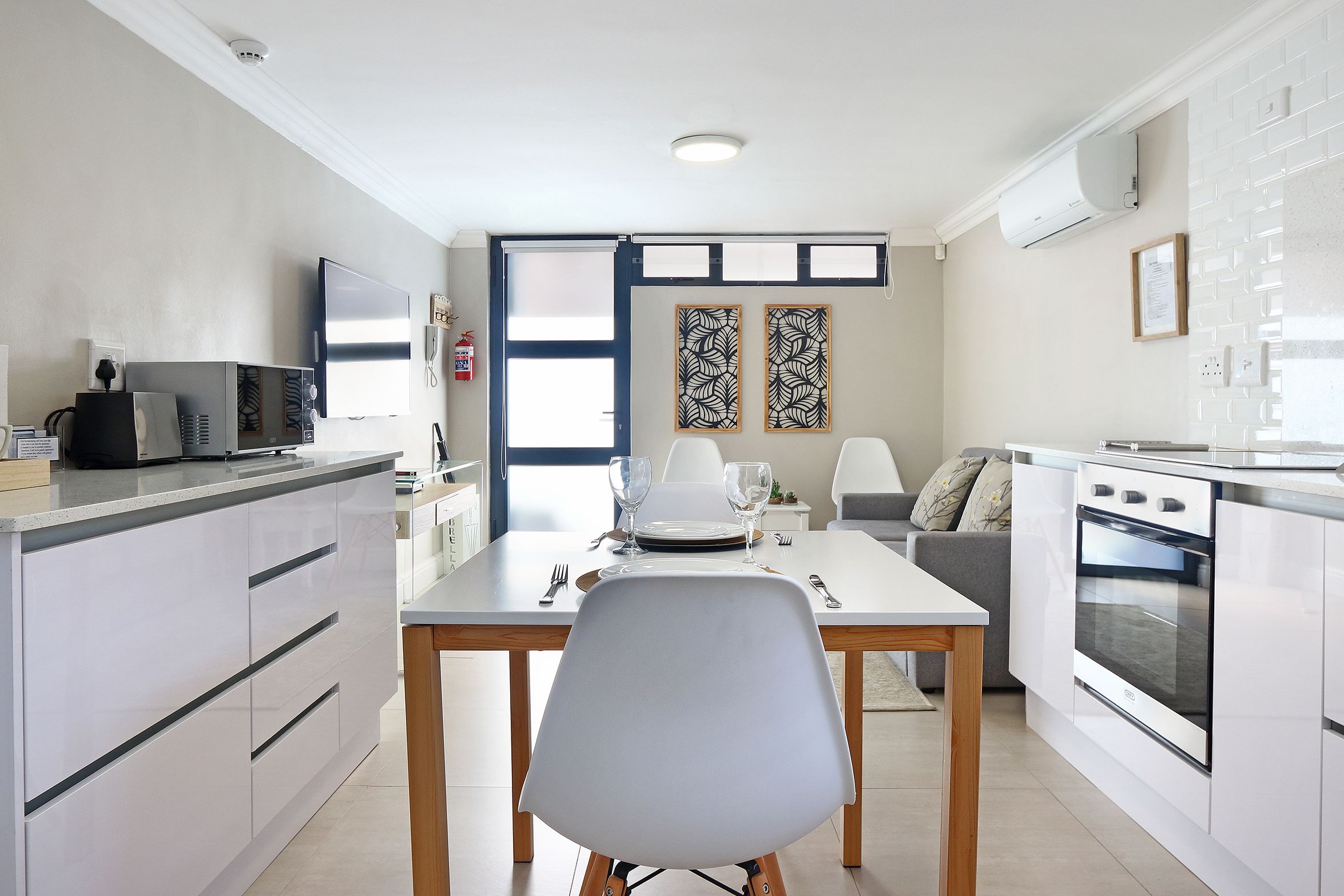 Una cocina moderna con armarios blancos, una mesa de comedor con sillas, un horno empotrado y un televisor de pantalla plana.