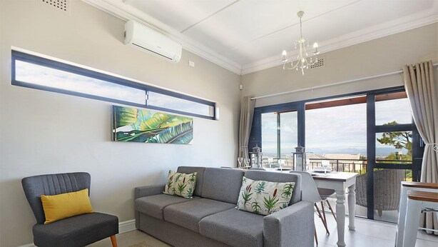 A modern living room with a grey sofa, a yellow armchair, and a dining area with a table and chairs. - Star Holiday Apartments (Cape Town)