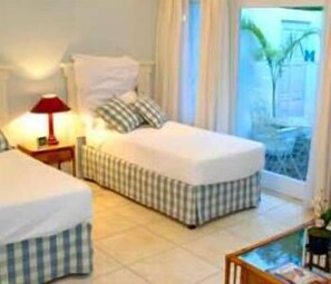 Quarto de hotel com duas camas, uma mesinha de cabeceira com abajur, uma pequena mesa e vista para o exterior.