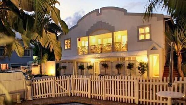 Une maison à deux étages avec une piscine, une clôture blanche en bois et des palmiers.