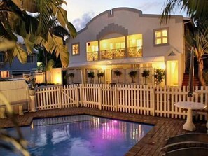 Une maison à deux étages avec une piscine, une clôture blanche en bois et des palmiers.