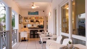 Un espace de restauration moderne, avec des meubles blancs, un bar doté d’étagères remplies de bouteilles, et une vue dégagée grâce à de grandes fenêtres.