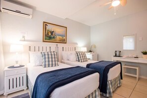 Une chambre d’hôtel avec deux lits, un bureau, une chaise, une petite table, un tableau au mur et un appareil de climatisation.