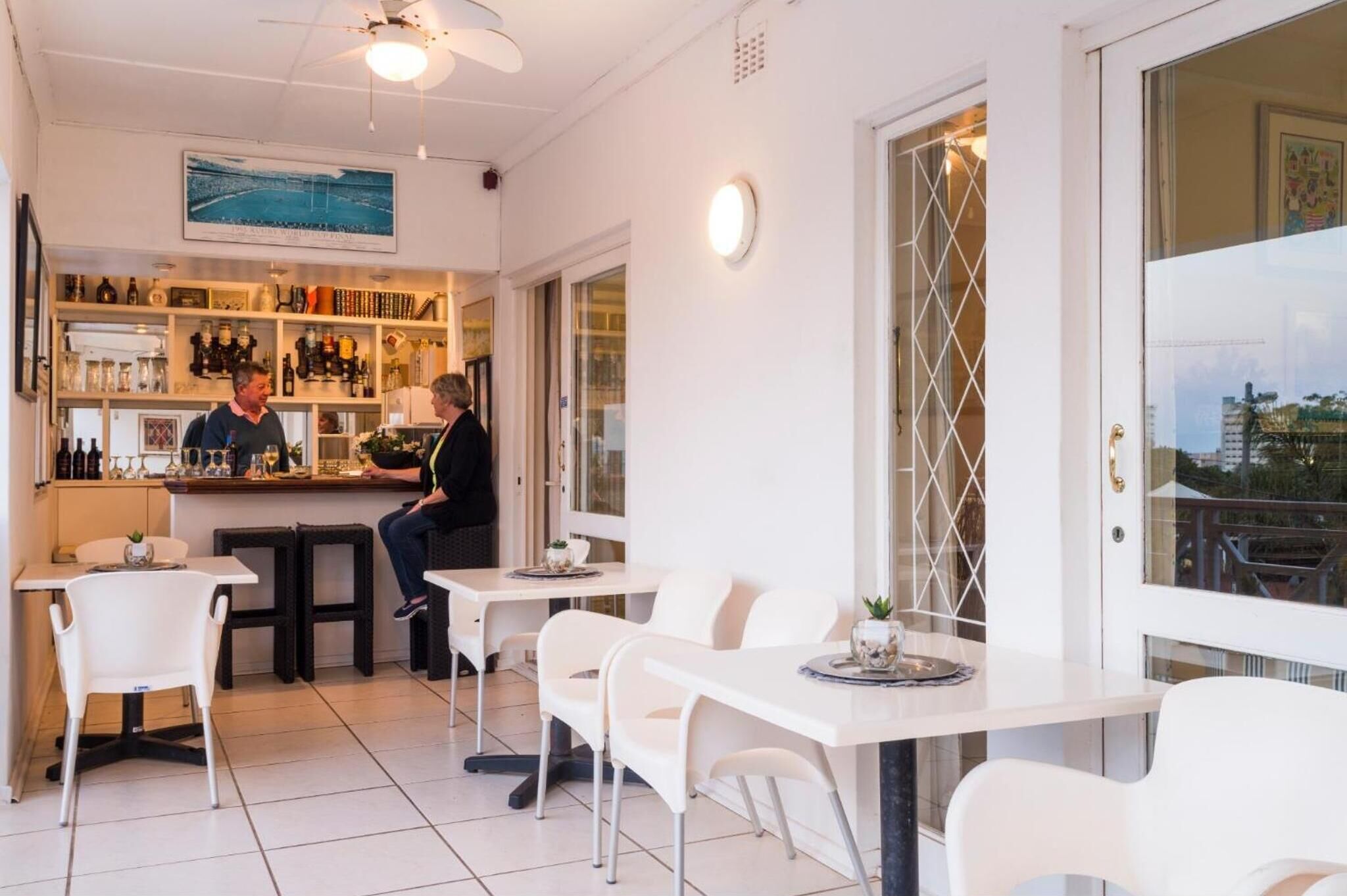 A modern bar area with white furniture and a bartender.