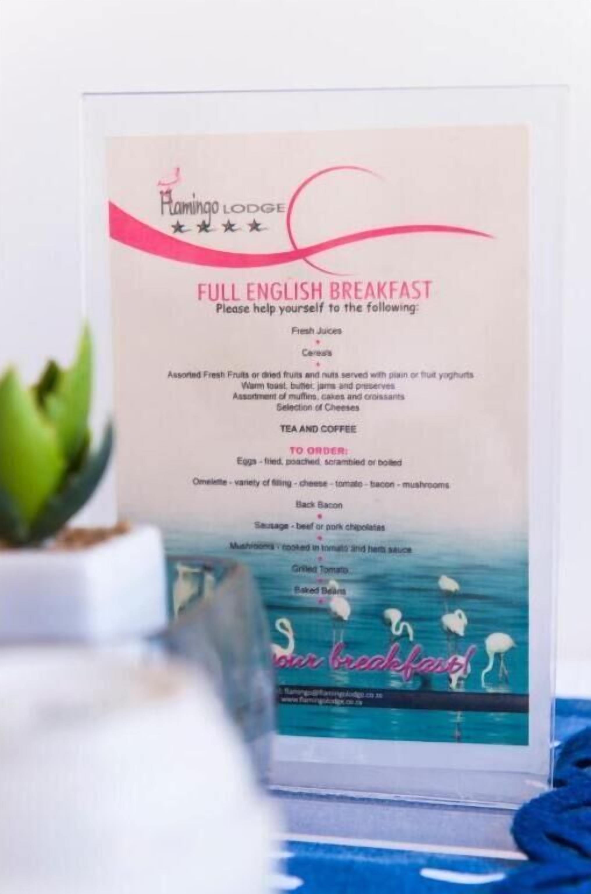 Pizarra de menú para un desayuno inglés completo en Flamingo Lodge, que incluye jugos frescos, frutas variadas, té, café, huevos, salchichas y más.