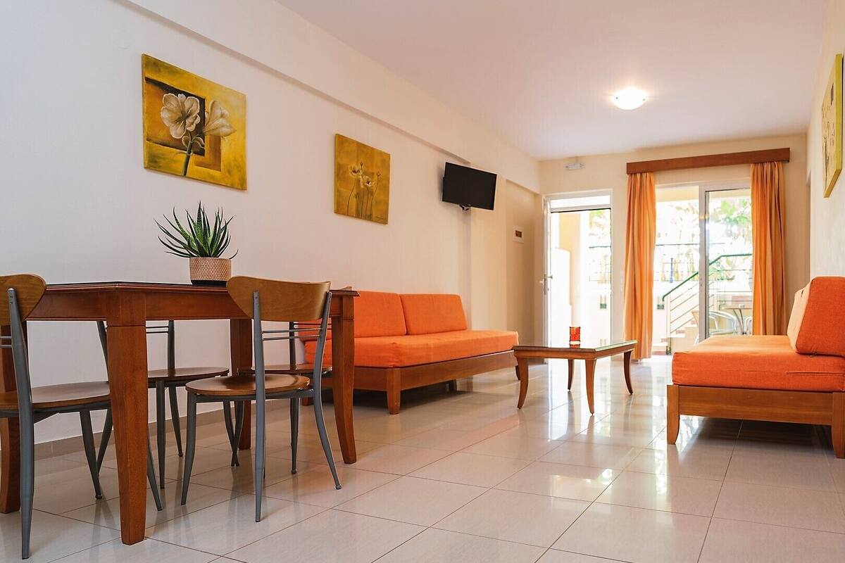 Un salon moderne avec une table à manger en bois, deux canapés orange et un téléviseur fixé au mur.