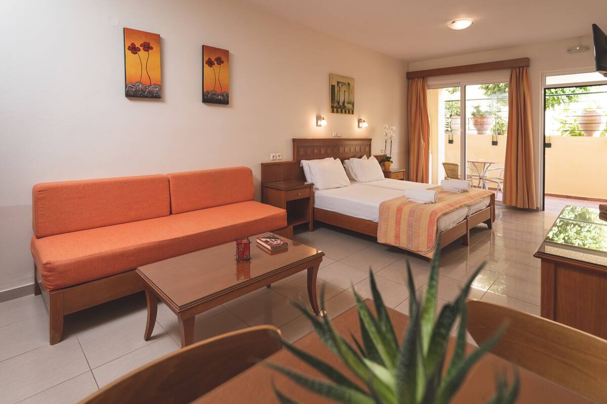 Une chambre d’hôtel avec un canapé, un lit recouvert d’une couverture à rayures, une table de chevet et une petite table sur laquelle est posée une plante.