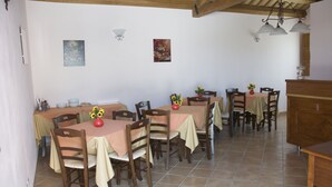 A dining area with multiple tables and chairs, wooden beams on the ceiling, and wall-mounted light fixtures. - Agriturismo Baglio Antico (Trapani)