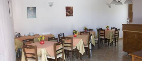 Un comedor con varias mesas y sillas, vigas de madera en el techo y lámparas fijadas a la pared.