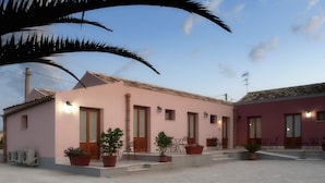 A pink building with multiple doors and windows, outdoor seating, and potted plants. - Agriturismo Baglio Antico (Trapani)