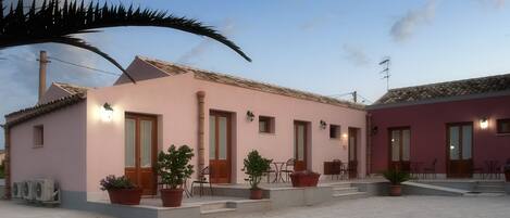 A pink building with multiple doors and windows, outdoor seating, and potted plants.