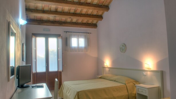 A bedroom with a bed, bedside tables, a desk with a computer, and a window with curtains. - Agriturismo Baglio Antico (Trapani)