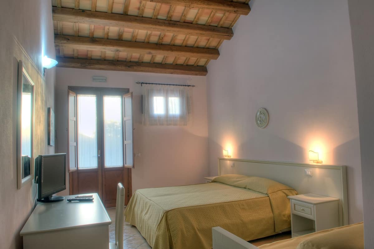 A bedroom with a bed, bedside tables, a desk with a computer, and a window with curtains.