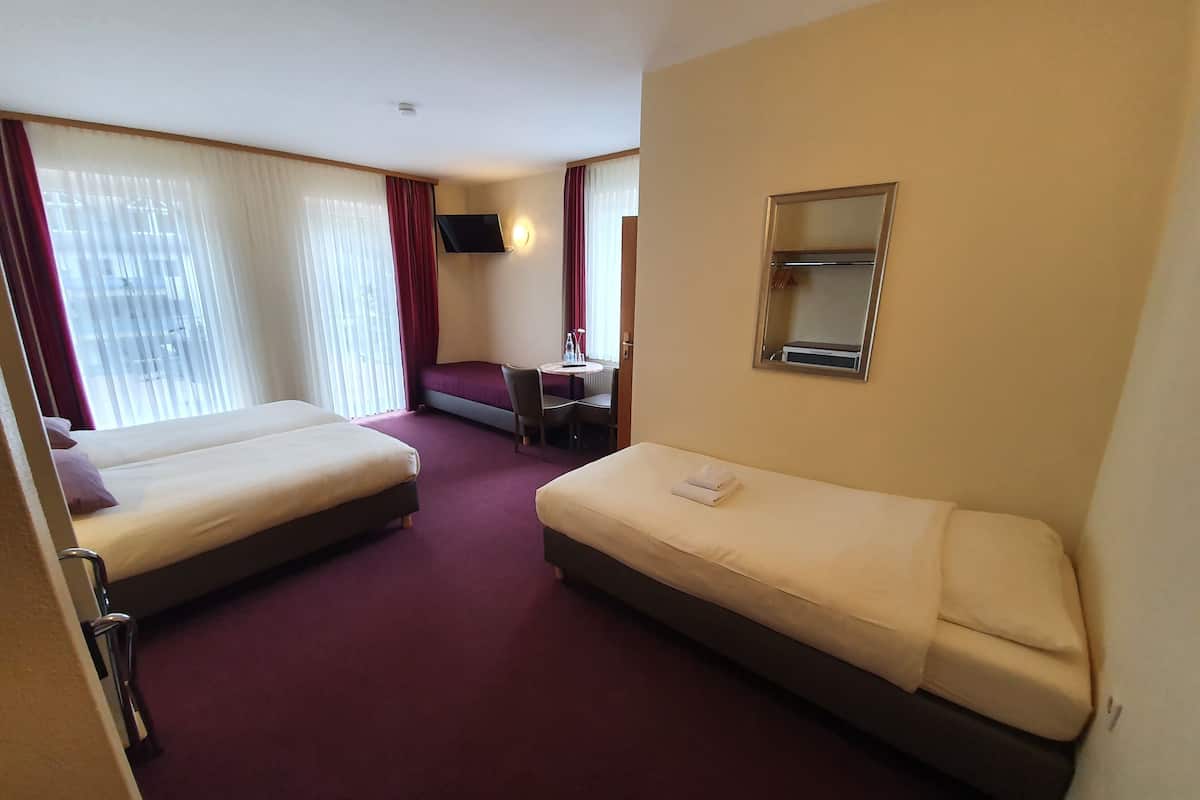 Une chambre d’hôtel avec deux lits, un canapé-lit, une petite table avec une chaise, un téléviseur fixé au mur et un miroir.