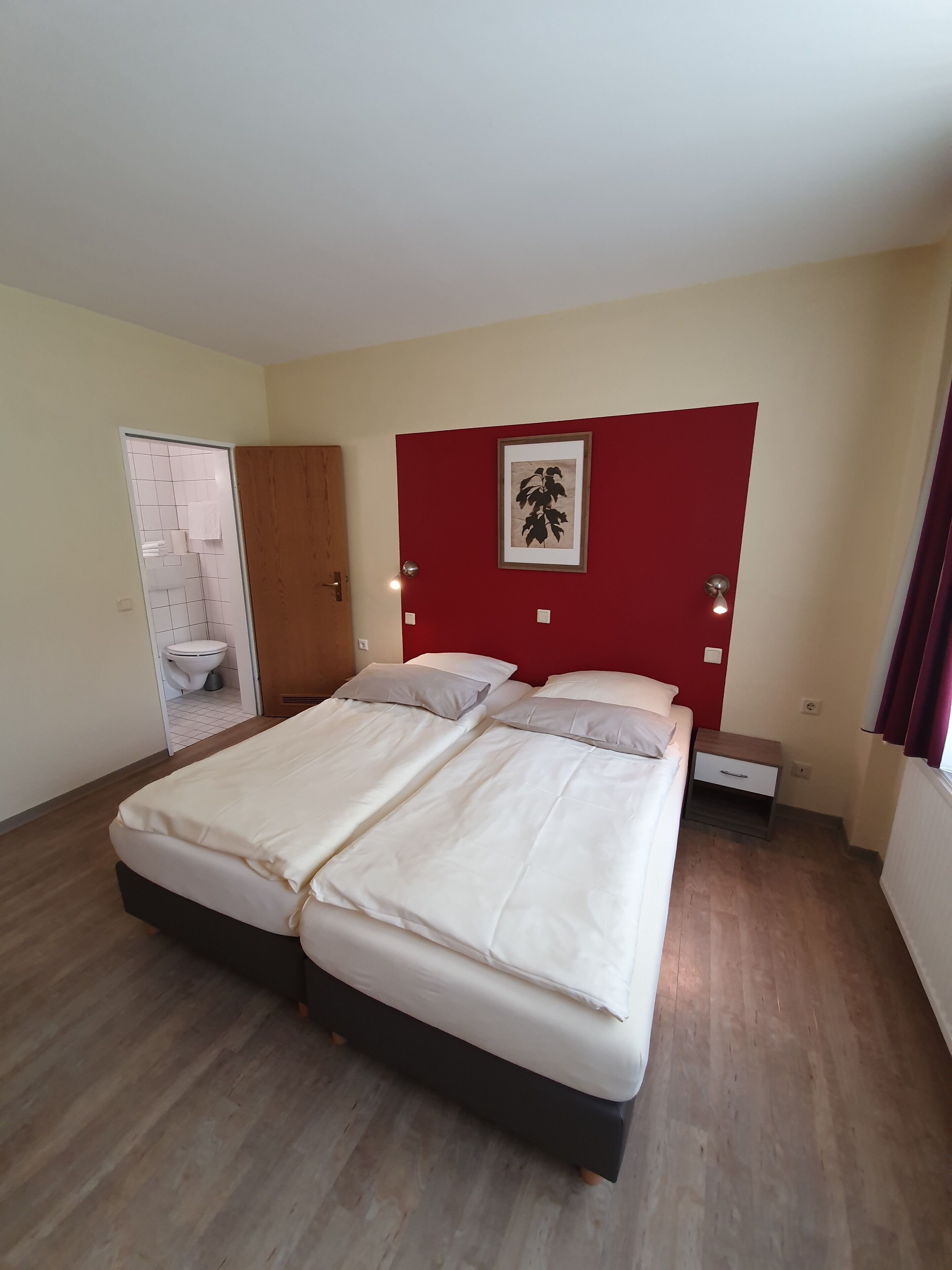 Un lit double avec un cadre en bois, une petite table de chevet et un luminaire fixé au mur.