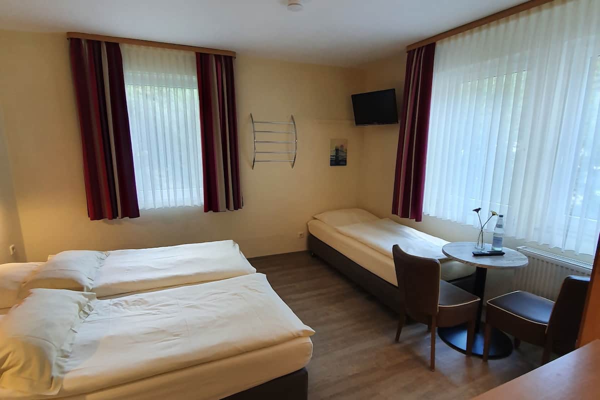 Une chambre d’hôtel avec deux lits, une petite table avec des chaises, un téléviseur fixé au mur et une fenêtre avec des rideaux.