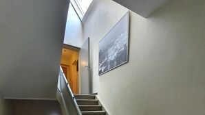 Una escalera con alfombra, barandilla, un cuadro en la pared y un letrero de salida de emergencia.
