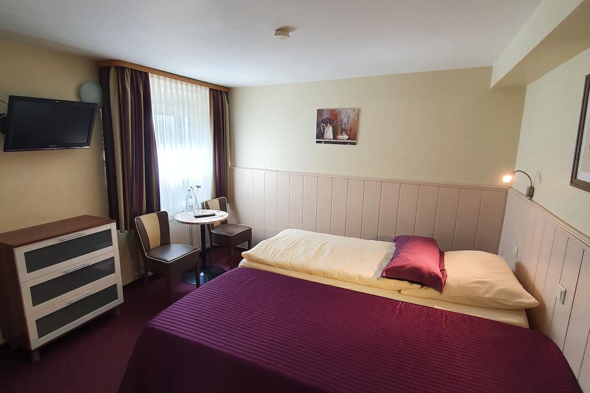 Une chambre d’hôtel avec un lit, un bureau, une chaise, une télévision et une fenêtre avec des rideaux.