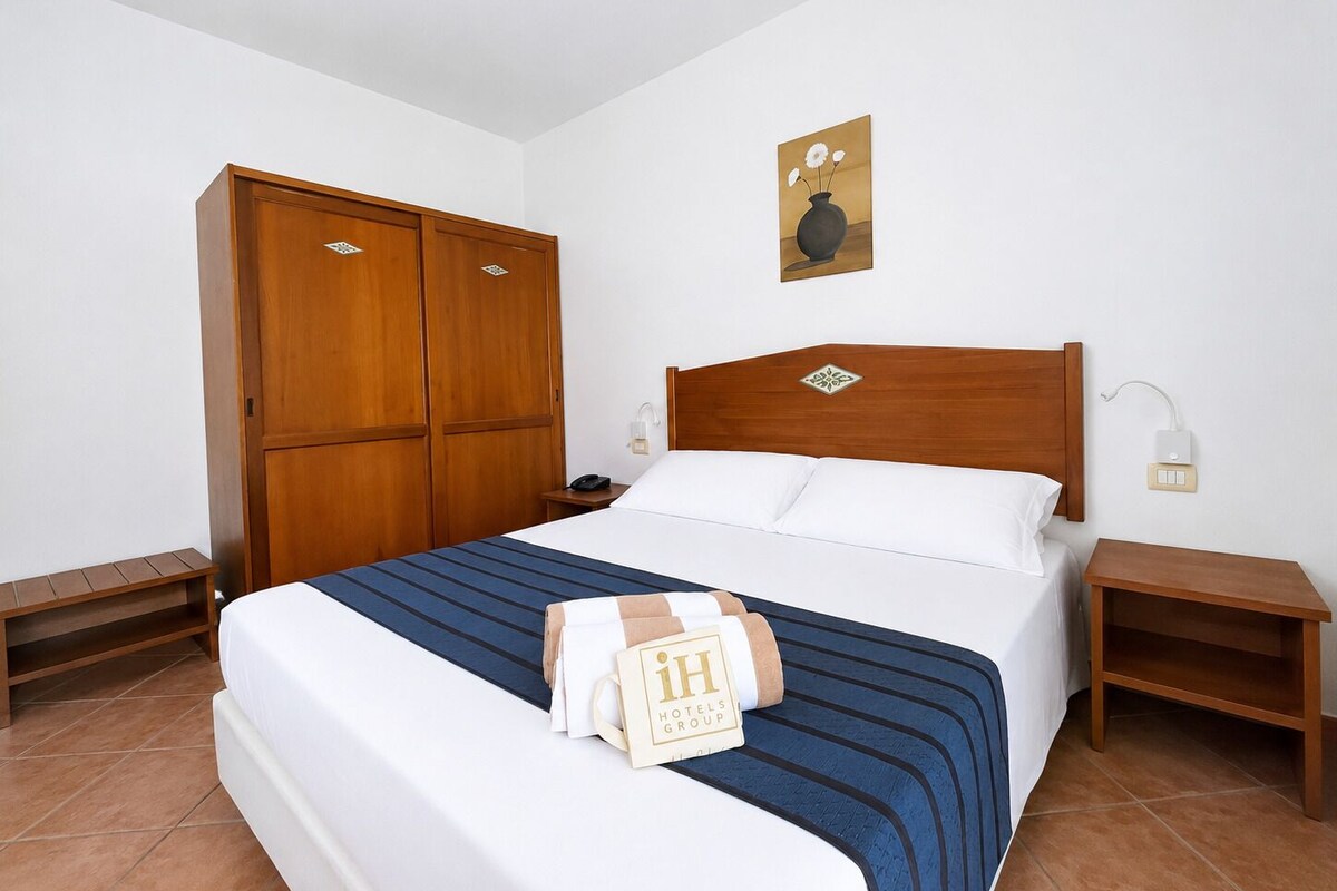Ein Hotelzimmer mit einem Bett, einem Holzschrank, Nachttischen, einer Nachttischlampe und einem gerahmten Bild.