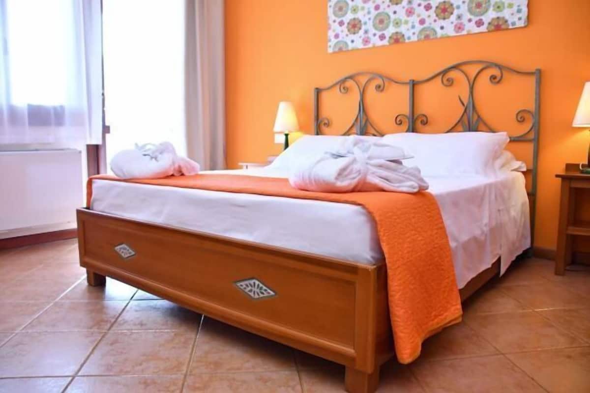 A bedroom with a bed, two bedside lamps, a window, and a wall with a floral pattern.
