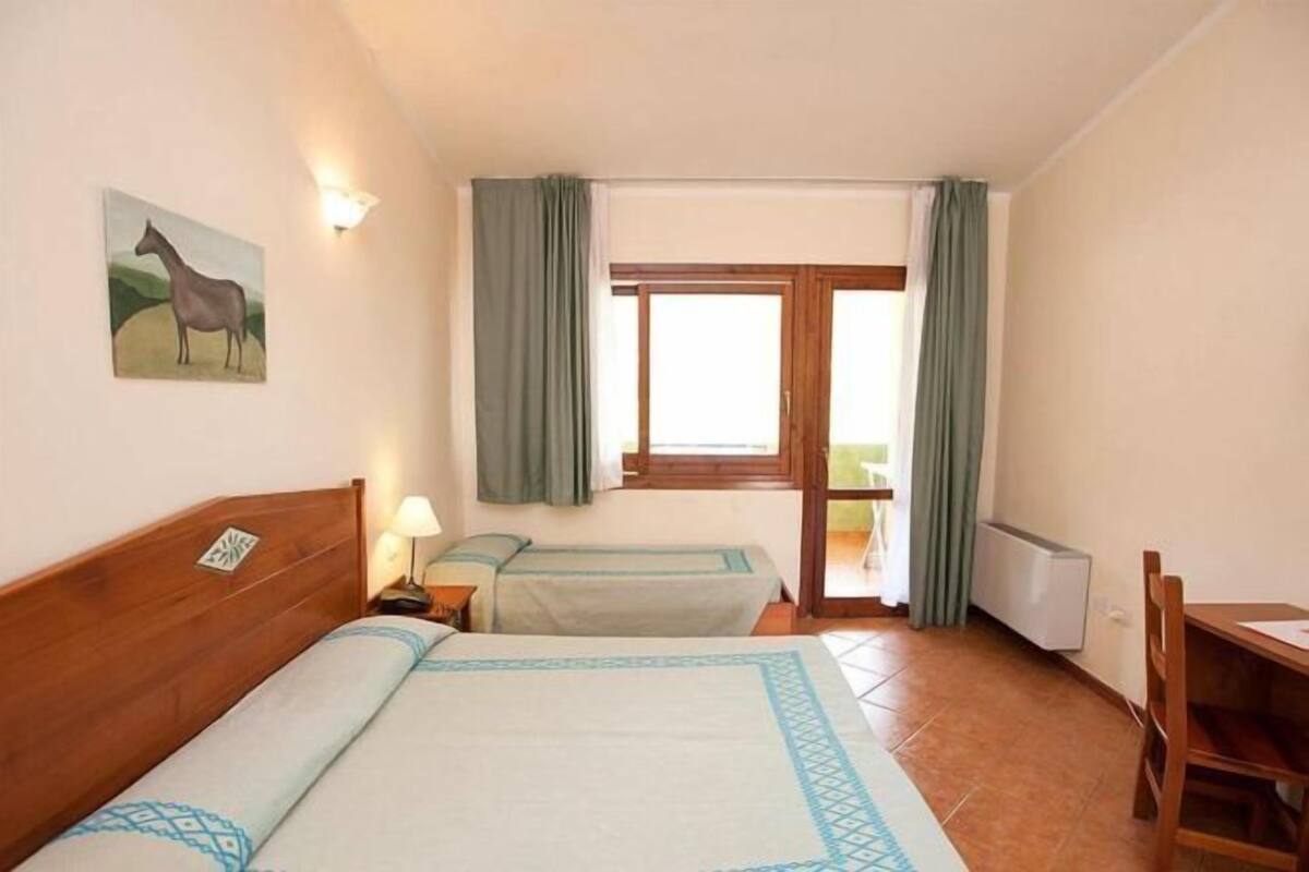 A hotel room with two beds, a window with curtains, a radiator, and a painting on the wall.