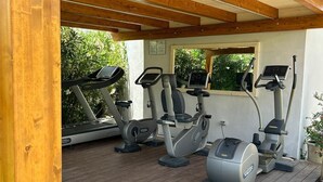 Zona de gimnasio al aire libre con equipo de ejercicio, suelo de madera y una maceta con flores.