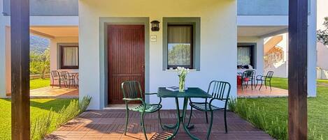 A wooden deck with a table and chairs, a door, and a window with a view.