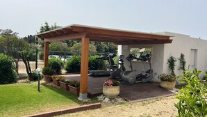 Un espacio al aire libre techado con equipo de ejercicios, que incluye una caminadora y bicicletas estáticas, bajo una pérgola de madera.