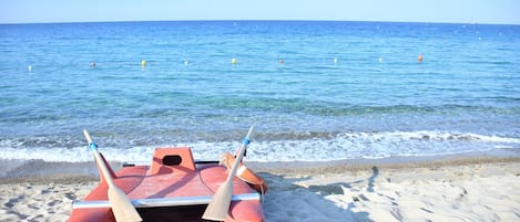 A red boat on a sandy beach with the ocean in the background.