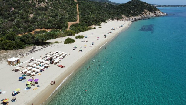 Una playa con agua turquesa cristalina, orilla arenosa y algunas sombrillas.