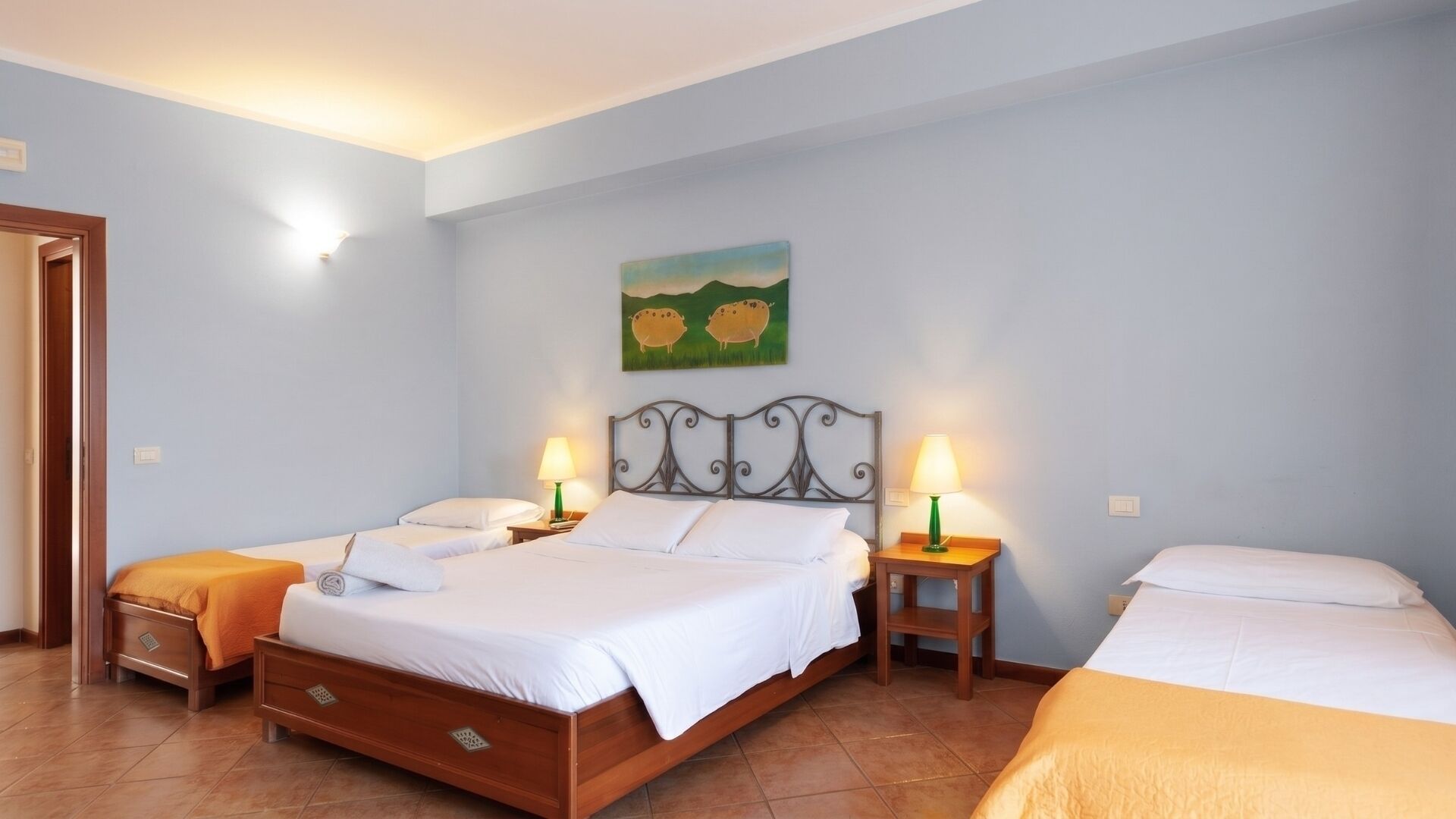 Hotellihuone, jossa on suuri sänky, kaksi yöpöytää, taulu seinällä ja ovi vasemmalla puolella.